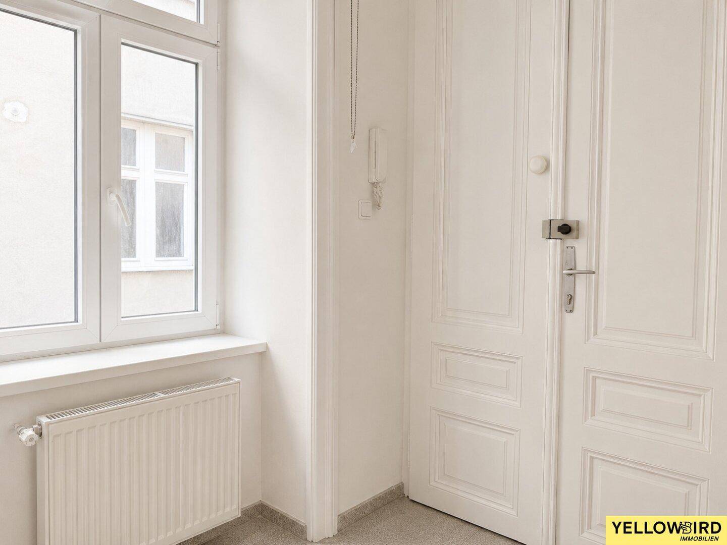 Flur mit Fenster und klassischer weißer Tür, die in einen Raum führt.