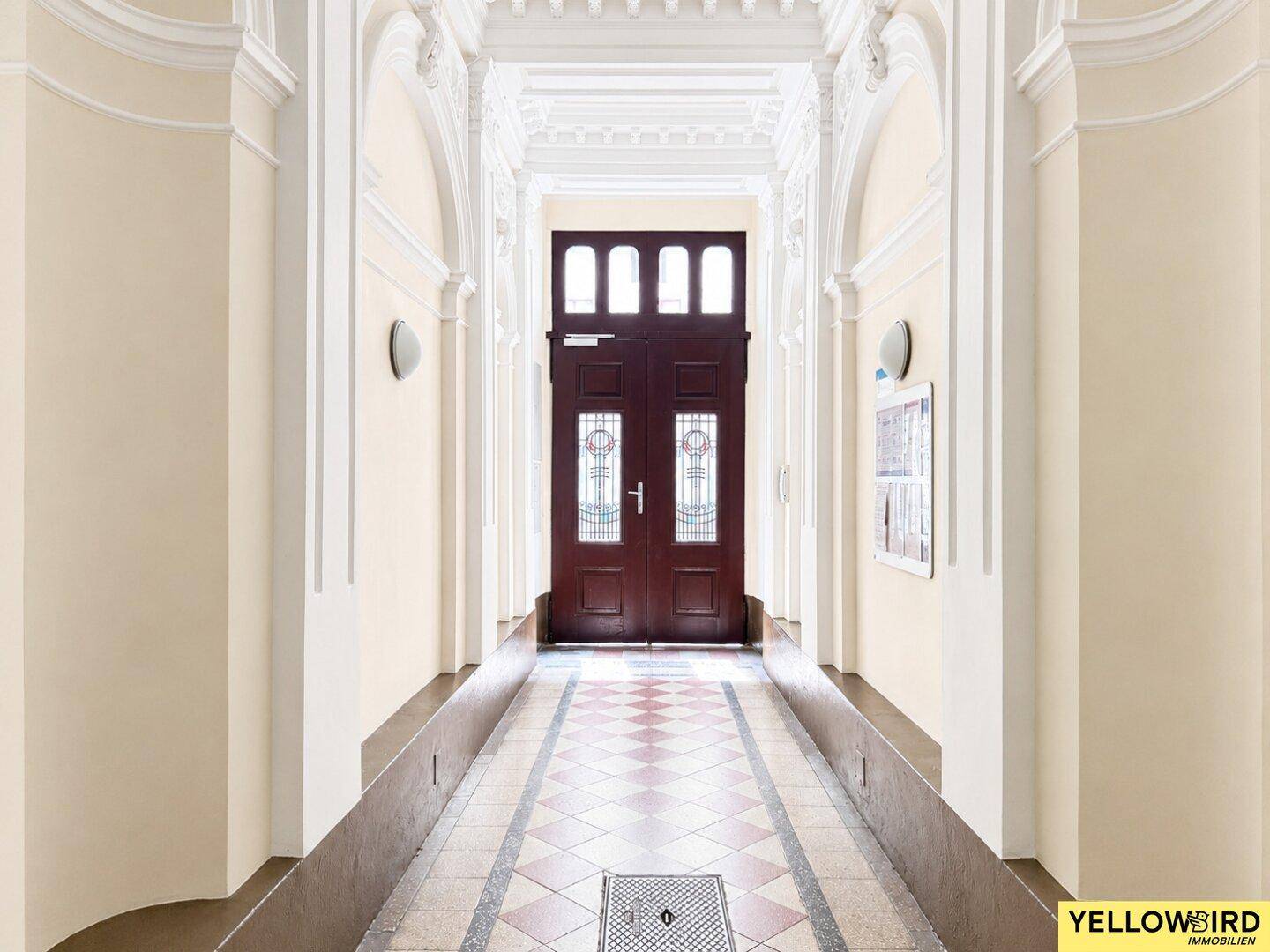 Historischer Flur in einem Altbau mit hohen Decken, Stuckverzierungen und einer großen Eingangstür.