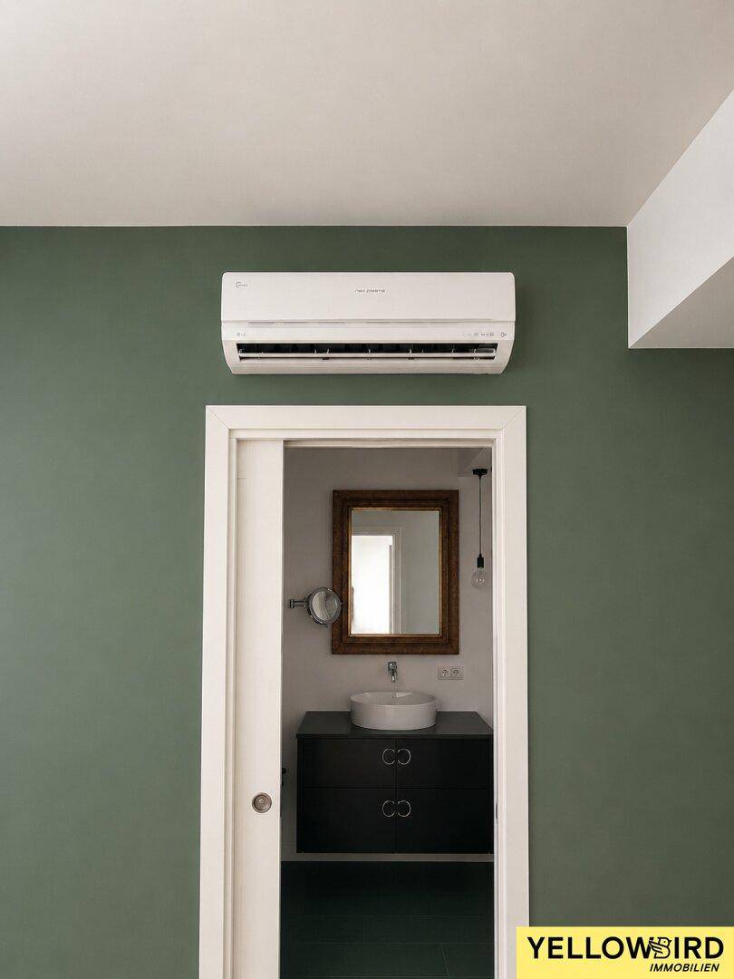 Flur mit Klimaanlage und Blick in ein modern gestaltetes Badezimmer mit Waschtisch.