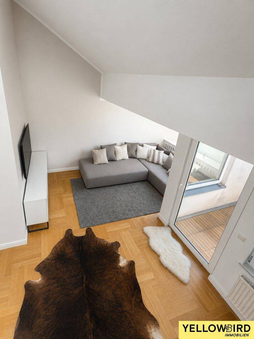 Offener Wohnbereich mit hohen Decken, Parkettboden und Blick auf den Balkon.