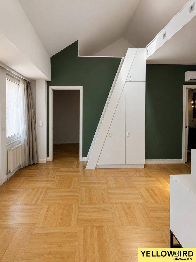 Heller Wohnbereich mit Parkettboden, grünen Akzentwänden und integrierten Schränken unter der Treppe.