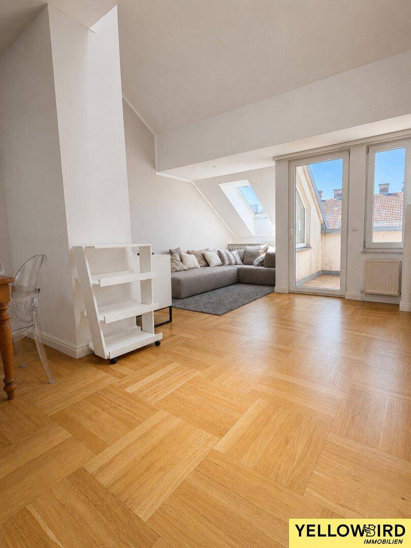 Geräumiges Wohnzimmer mit Fischgrätparkett, viel Tageslicht und Blick auf den Balkon.