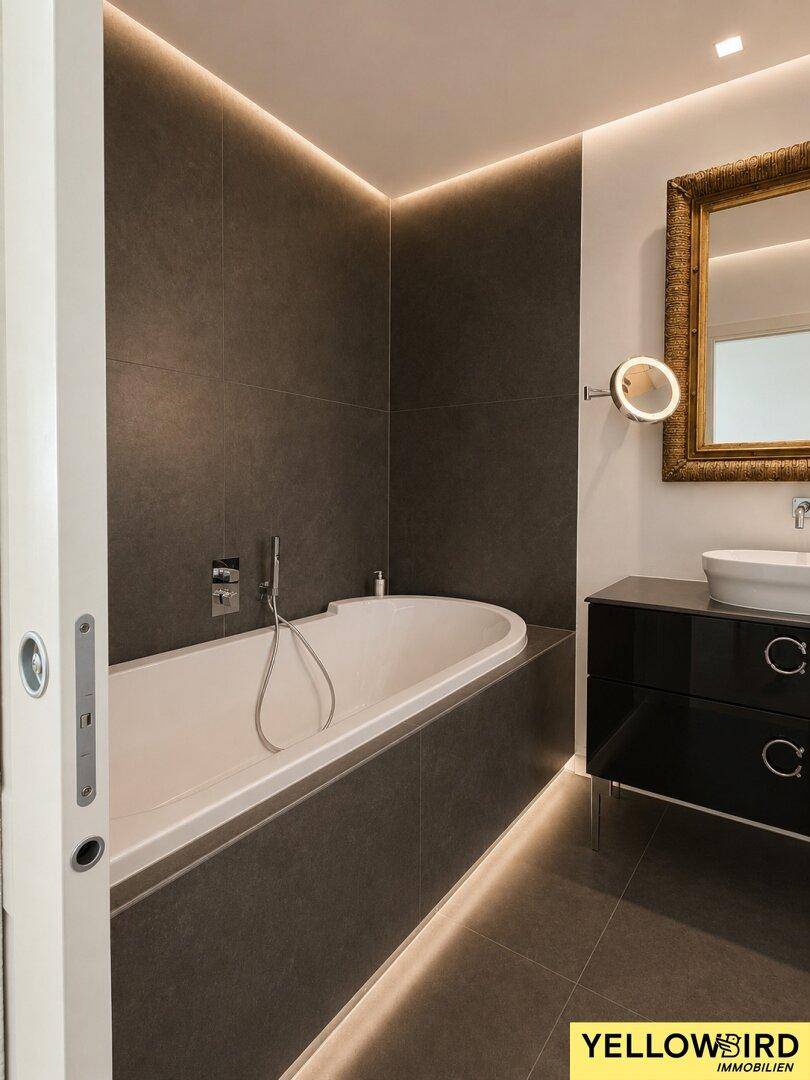 Stilvolles Badezimmer mit integrierter Badewanne, indirekter Beleuchtung und modernem Waschtisch.