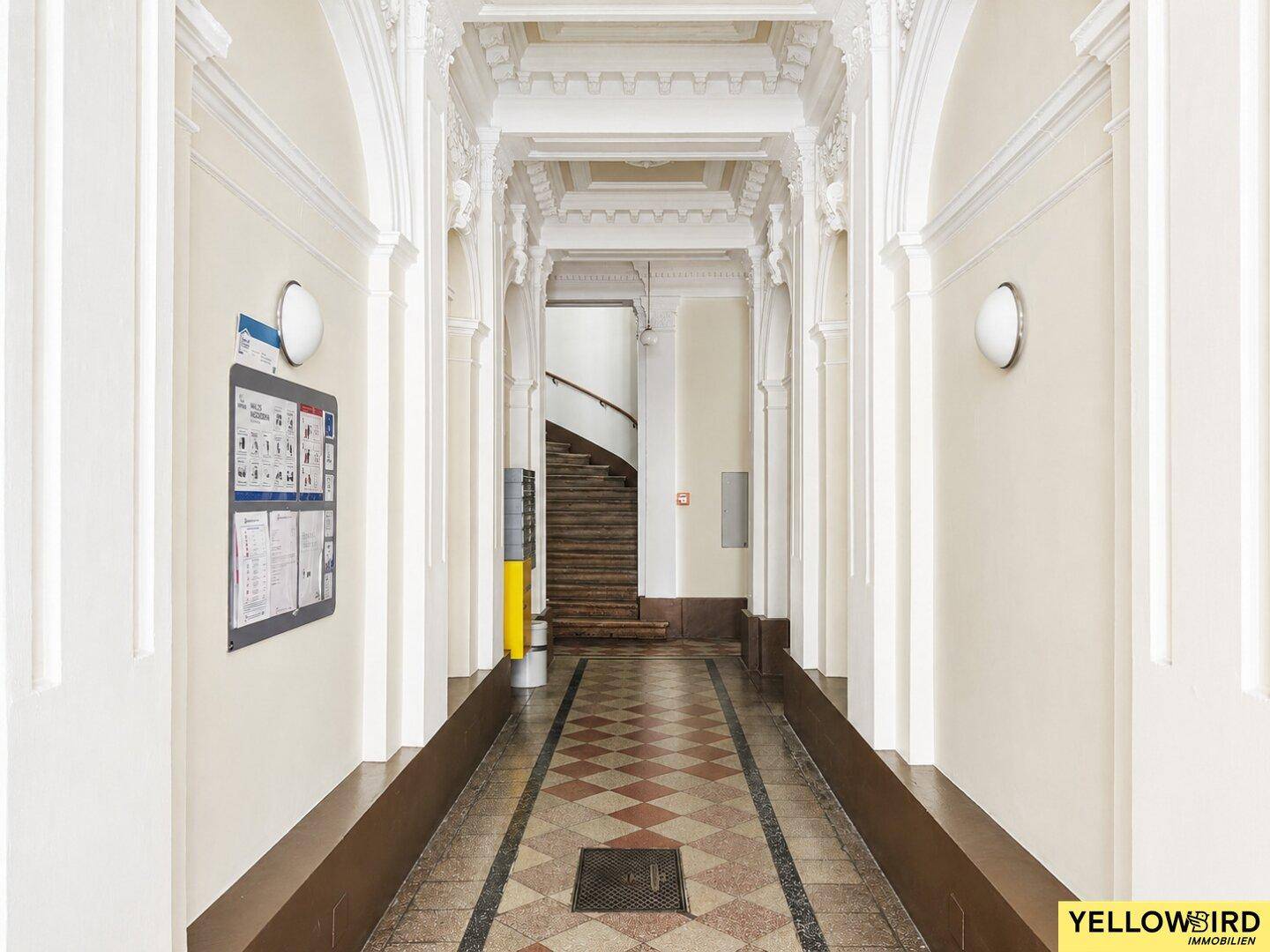 Langer, eleganter Flur in einem Altbau mit hohen Decken, Stuckverzierungen und gemustertem Boden.