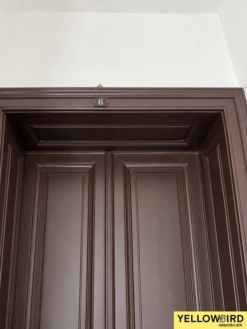 Detailansicht einer dunklen Holztür mit der Nummer 6, die zu einer Wohnung führt.