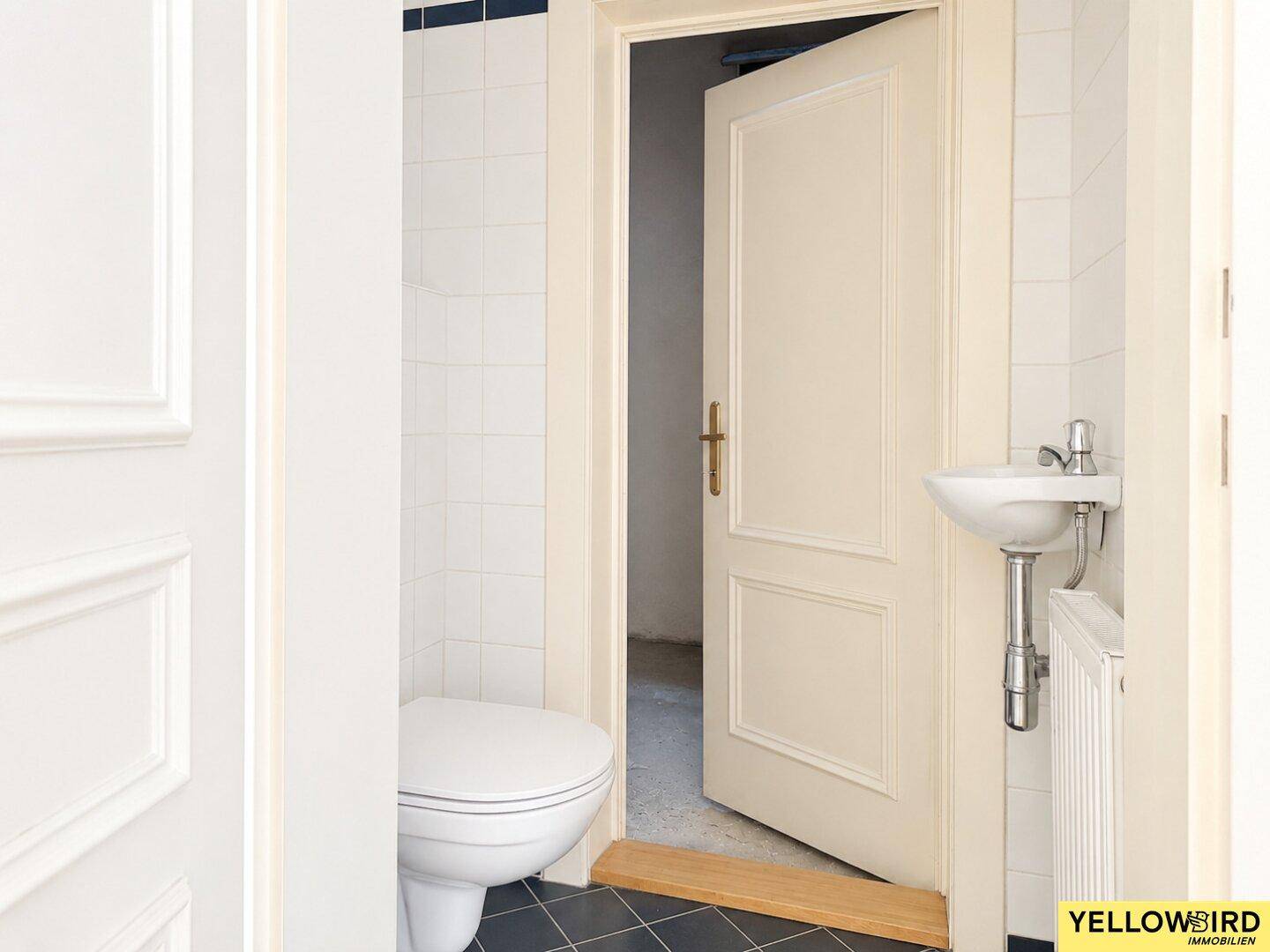 Helles Gäste-WC mit Wand-WC, kleinem Waschbecken und dunklen Bodenfliesen.