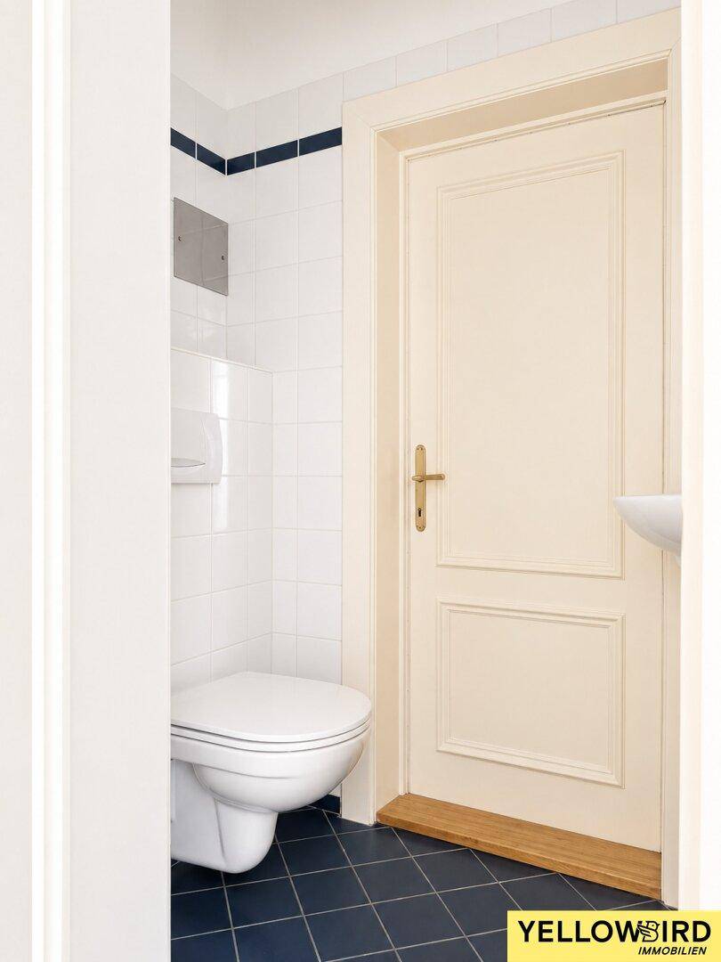 Kompaktes Gäste-WC mit Wand-WC, kleinem Waschbecken und dunklen Fliesen auf dem Boden.