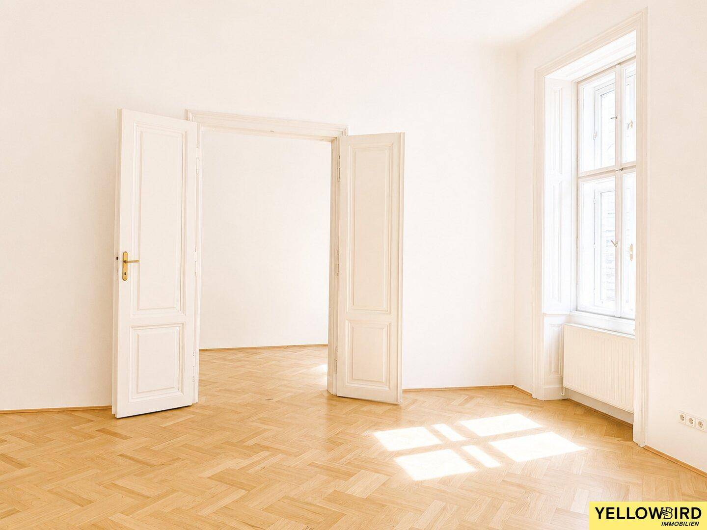Offener Raum mit Fischgrätparkett und hohen Doppeltüren, die zu einem weiteren Zimmer führen.