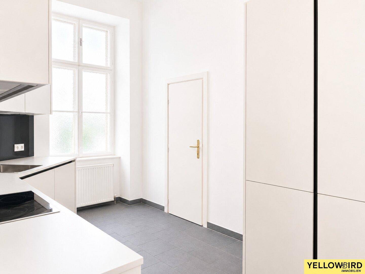 Moderne Küche mit weißen Schränken, dunklem Fliesenspiegel und einem Fenster, das Tageslicht spendet.