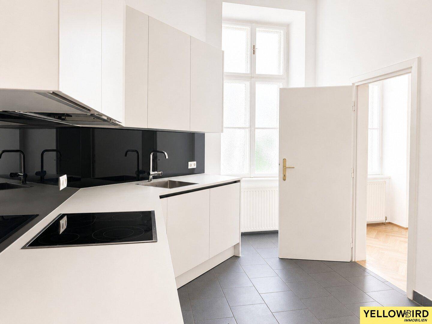 Helle, moderne Küche mit weißen Schränken, dunklem Fliesenspiegel und integriertem Kochfeld.