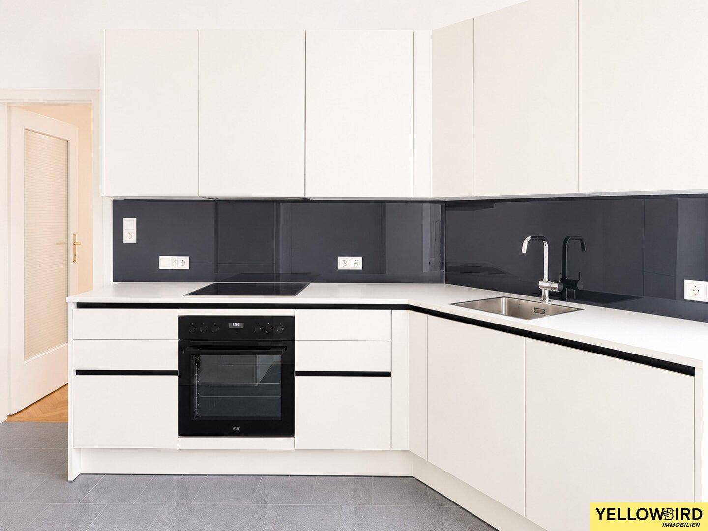 Voll ausgestattete, moderne Küche mit weißen Schränken, integriertem Backofen und dunklem Fliesenspiegel.