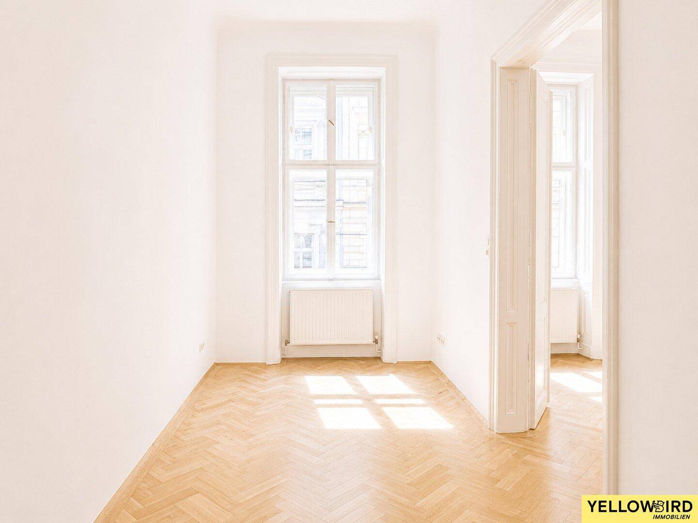 Leerer Raum mit klassischem Fischgrätparkett und einem hohen Fenster, das den Raum mit Licht füllt.