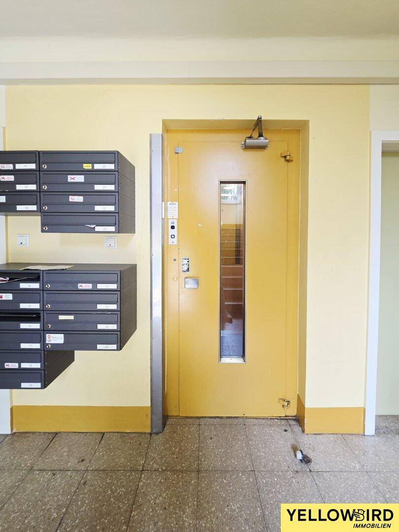 Eingangsbereich mit gelben Wänden, Terrazzoboden, Briefkästen und Aufzugstür.