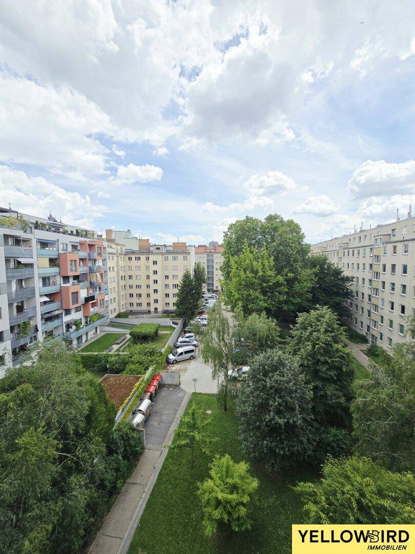 Luftaufnahme einer Wohngegend mit Gebäuden, Bäumen und parkenden Fahrzeugen unter bewölktem Himmel.