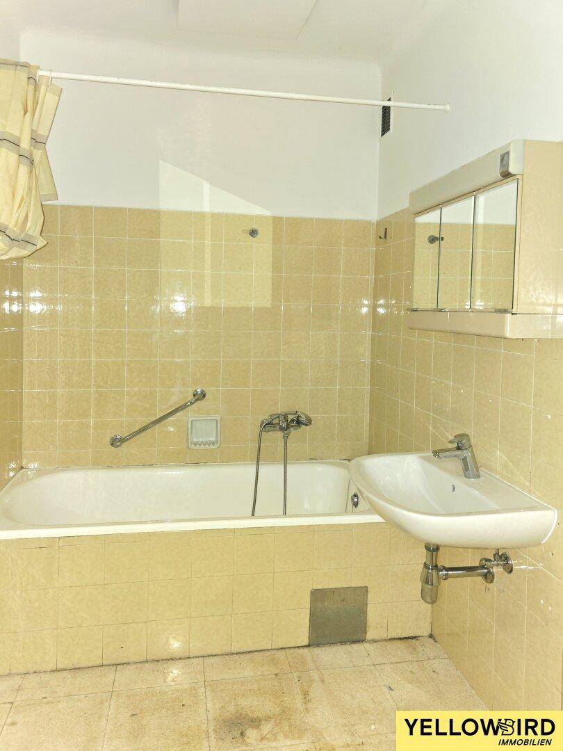 Badezimmer mit gelben Fliesen, Badewanne, Waschbecken und Spiegelschrank.