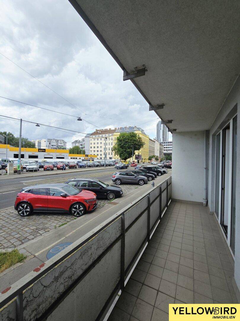 Balkon mit Fliesenboden und Blick auf die Straße mit parkenden Autos und umliegende Gebäude.