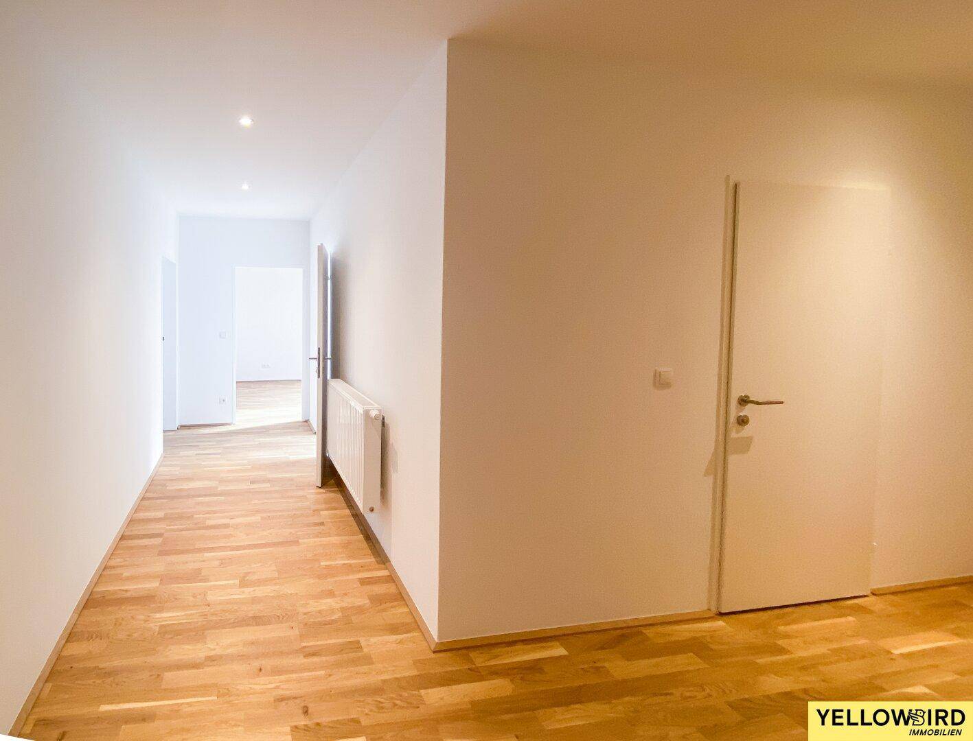 Langer, heller Flur mit Parkettboden und Heizkörper, der verschiedene Zimmer der Wohnung verbindet.
