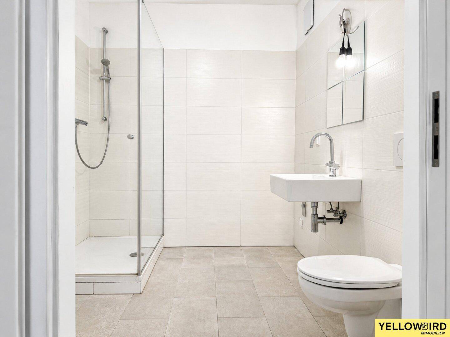 Modernes Badezimmer mit Dusche, WC und Waschbecken, hell gefliest.