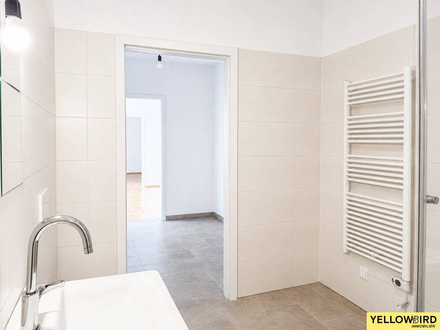 Helles Badezimmer mit Handtuchheizkörper und Blick in den angrenzenden Raum.