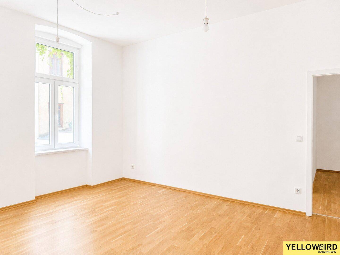 Geräumiger, heller Wohnraum mit Laminatboden und Zugang zu einem weiteren Zimmer.
