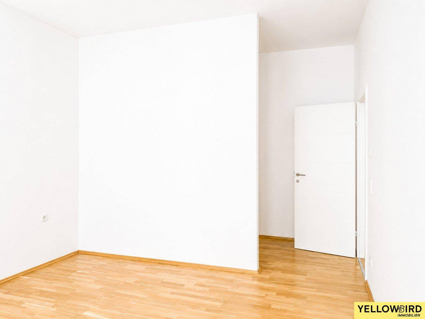 Leerer Raum mit weiß gestrichenen Wänden und hellem Laminatboden.
