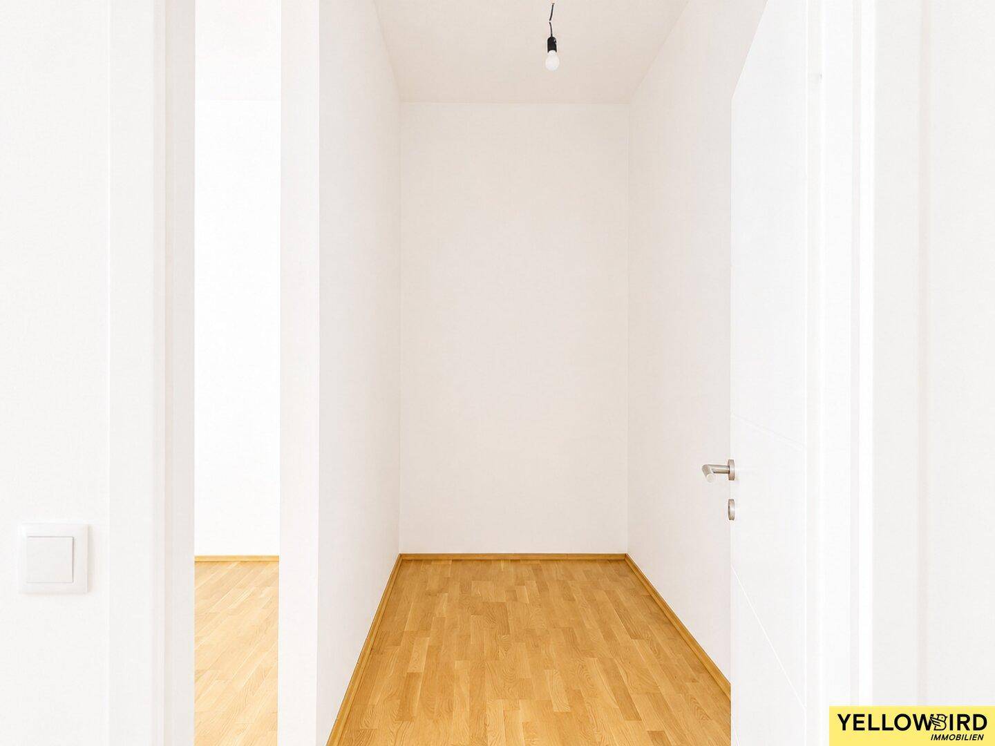 Schmaler Flur mit Laminatboden und weißer Tür, der zu weiteren Räumen führt.