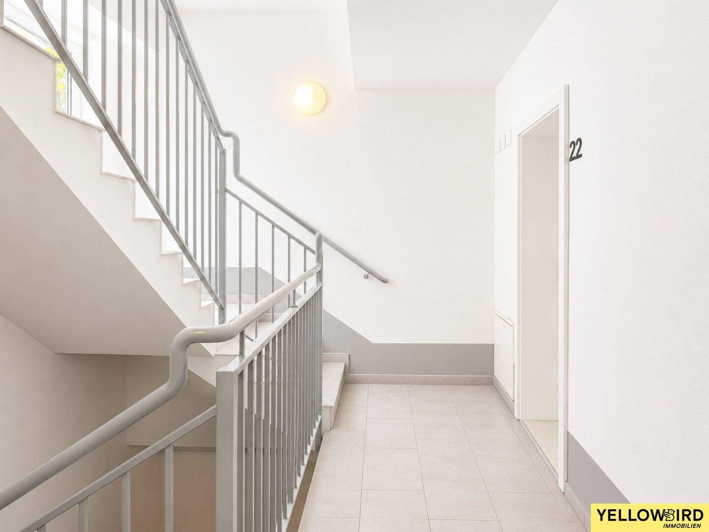 Treppenhaus mit grauem Geländer und Fliesenboden, führt zu den oberen Etagen.