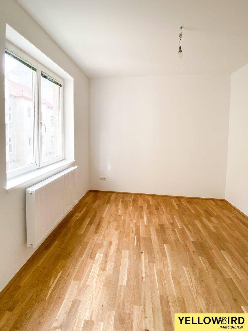 Helles Zimmer mit Parkettboden und Fenster, das einen Blick auf die städtische Umgebung bietet.