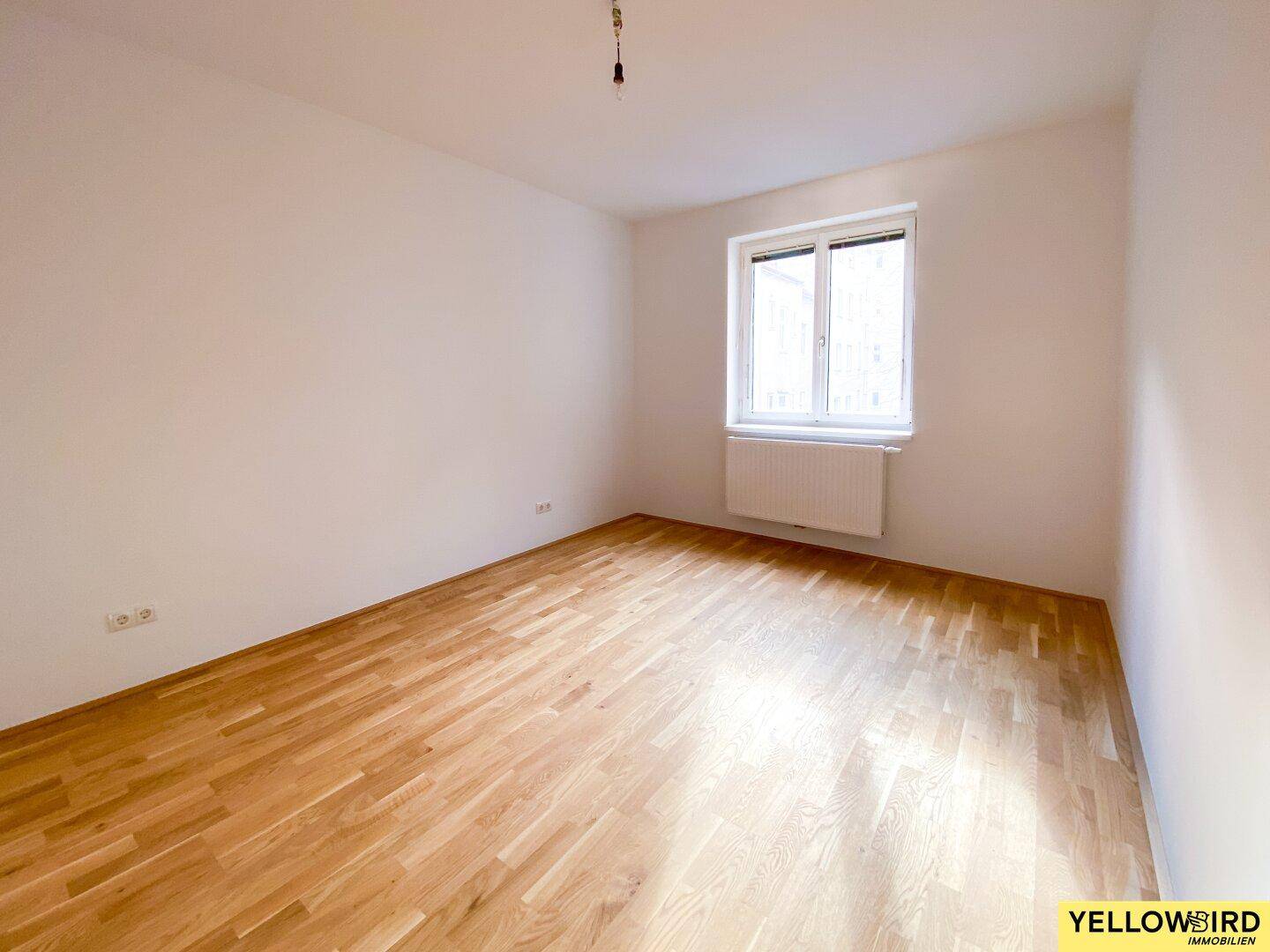 Geräumiges Zimmer mit hellem Parkettboden und großen Fenstern, ideal für Schlaf- oder Wohnbereich.