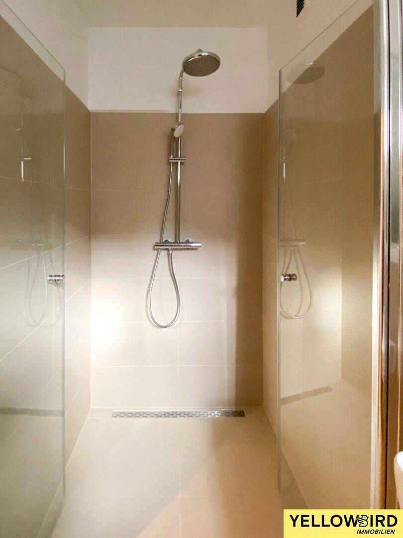 Moderne Duschkabine mit Glaswänden und beigefarbenen Fliesen, ausgestattet mit einer Regendusche.