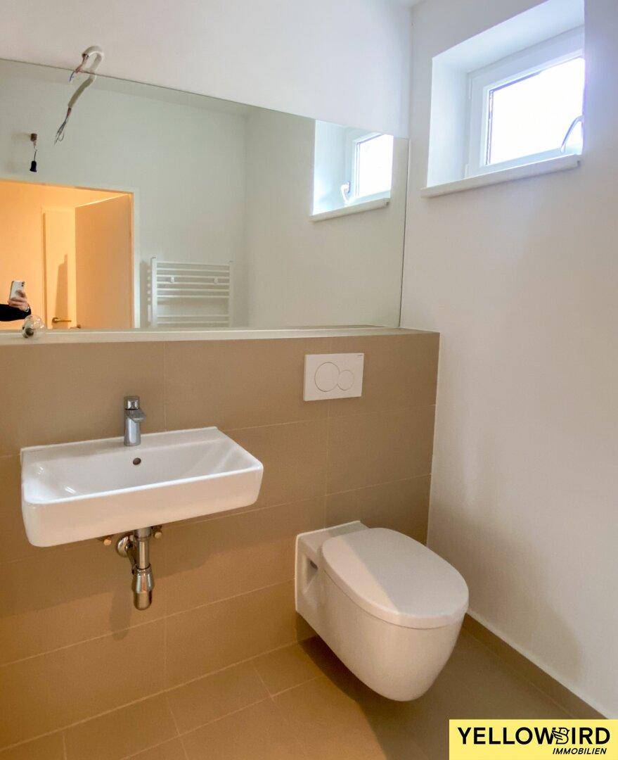 Modernes Badezimmer mit wandhängendem WC, Einzelwaschbecken und großem Spiegel über dem Waschtisch.
