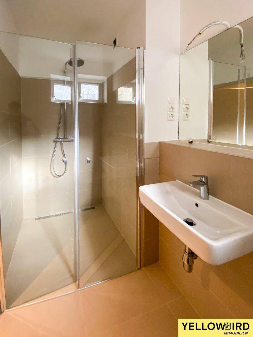 Helles Badezimmer mit begehbarer Dusche, Einzelwaschbecken und großem Spiegel, modern gefliest.