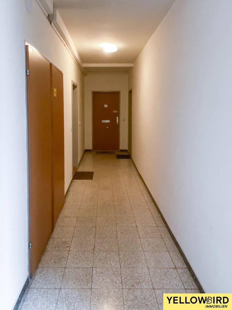 Langer, gefliester Hausflur mit Schränken und Eingangstür, führt zu den Wohneinheiten des Gebäudes.