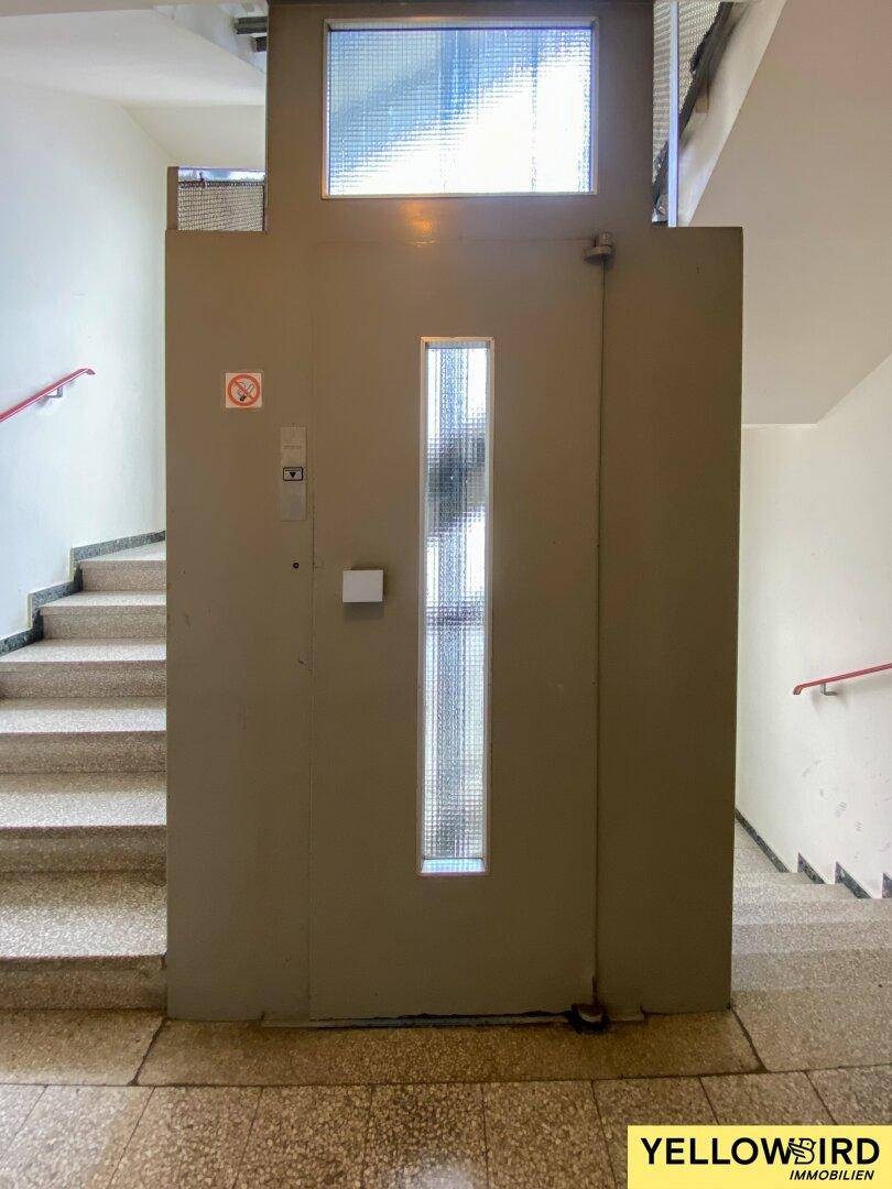 Treppenhaus mit Aufzug und Terrazzoboden, verbindet die verschiedenen Etagen des Mehrfamilienhauses.