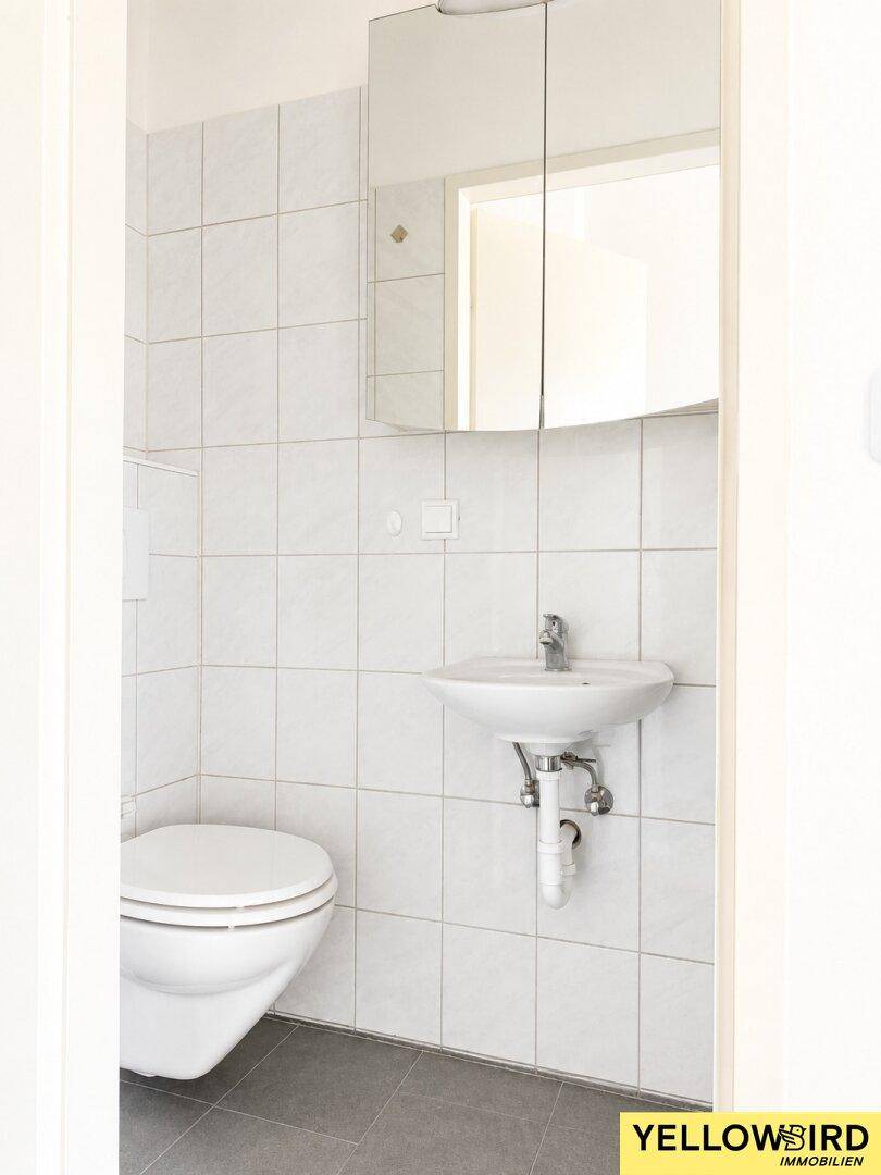 Kleines WC mit wandhängender Toilette, Waschbecken und hellen Fliesen, praktisch und funktional.