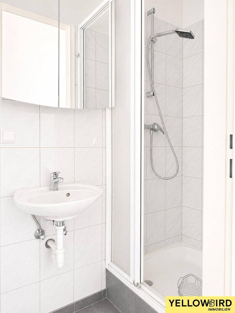 Modernes Badezimmer mit Duschkabine, Waschbecken und hellen Wandfliesen sowie dunklem Boden.