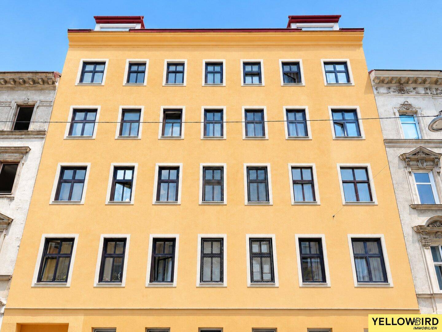 Gelbe Gebäudefassade mit zahlreichen Fenstern und klassischer Architektur in urbaner Umgebung.