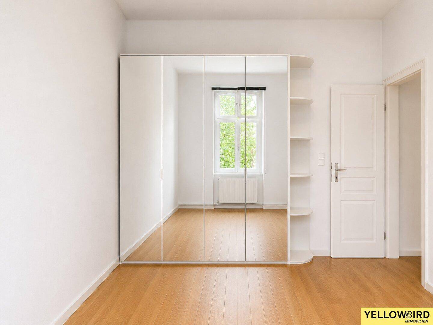Schlafzimmer mit großem Spiegelschrank und Parkettboden, das viel Tageslicht durch das Fenster erhält.