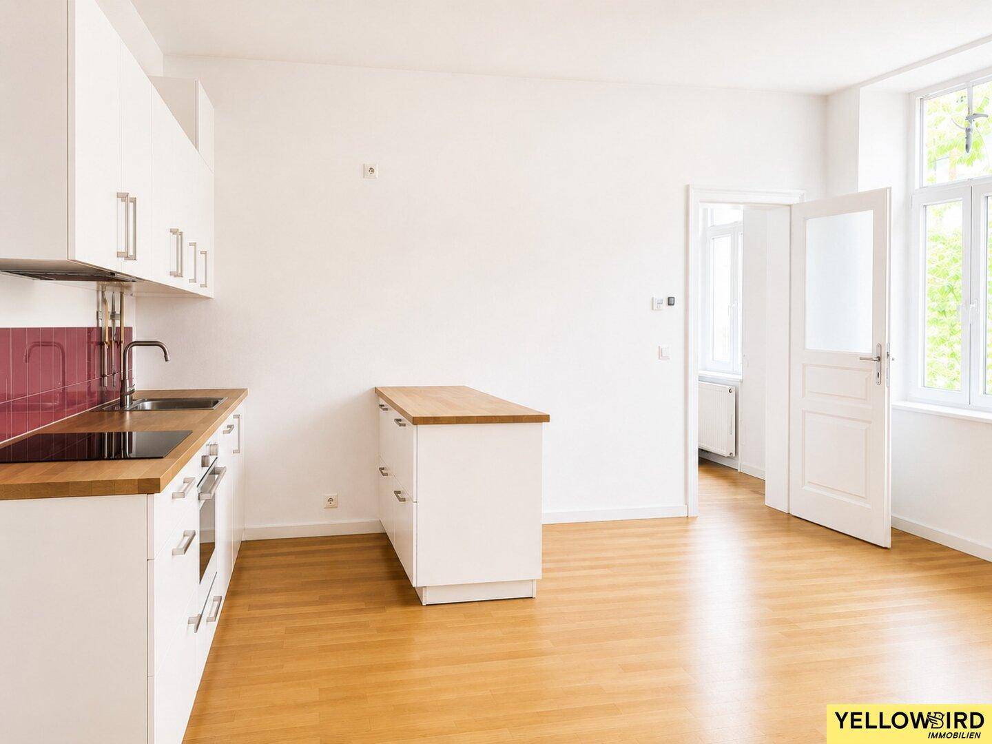 Offene Küche mit weißen Schränken, Holztheke und Parkettboden, bereit für die Einrichtung.