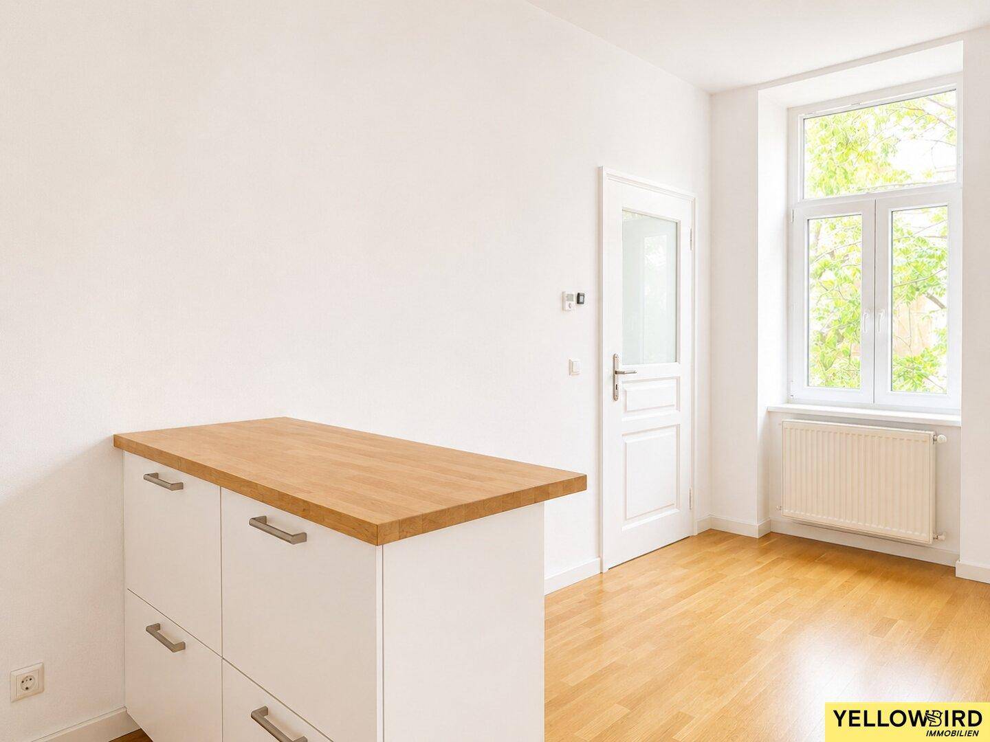 Kücheninsel mit Holzplatte und Stauraum, ergänzt durch ein helles Fenster und Parkettboden.