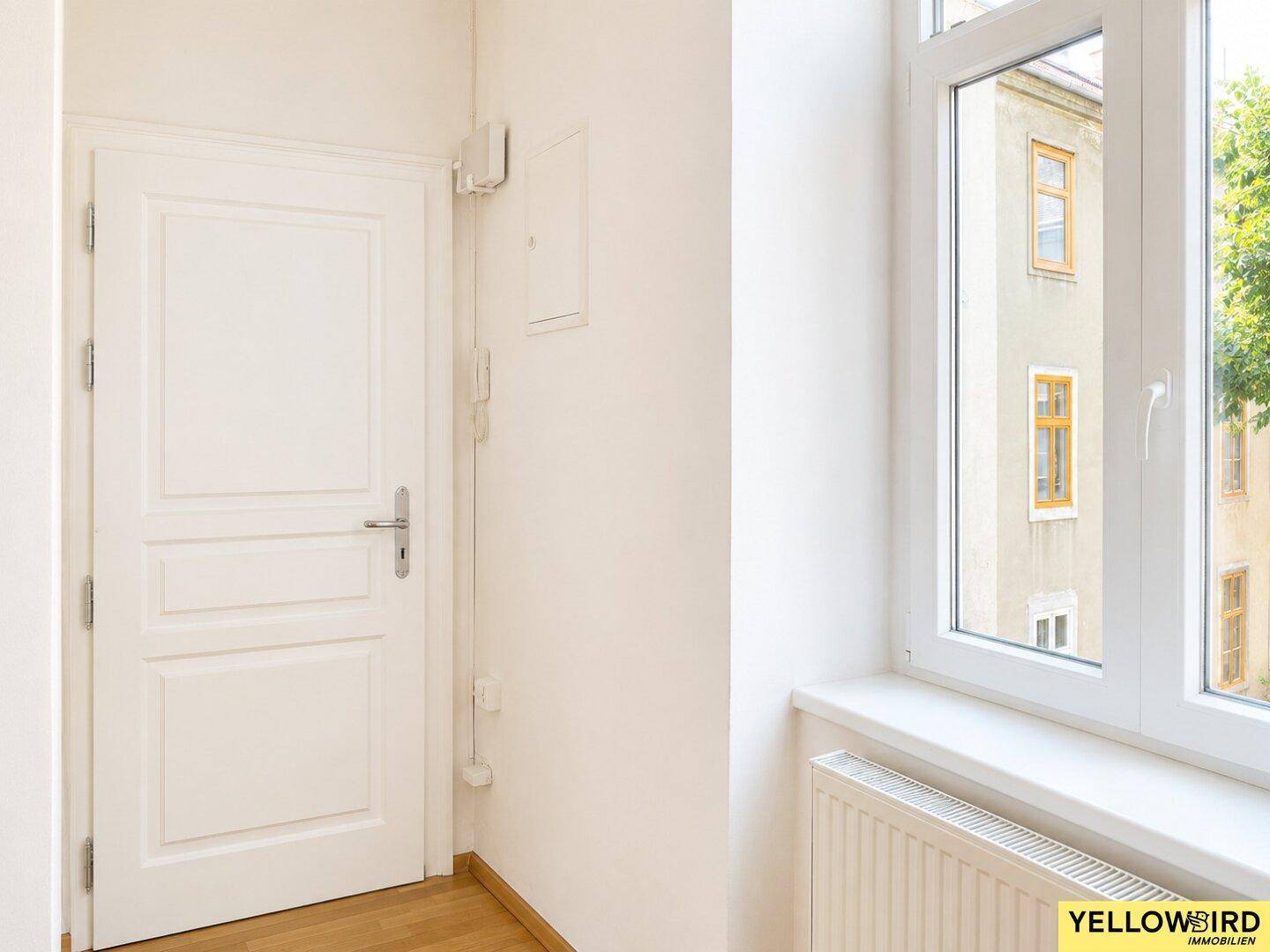 Heller Flur mit Parkettboden und einem Fenster, das den Blick auf den Innenhof freigibt.