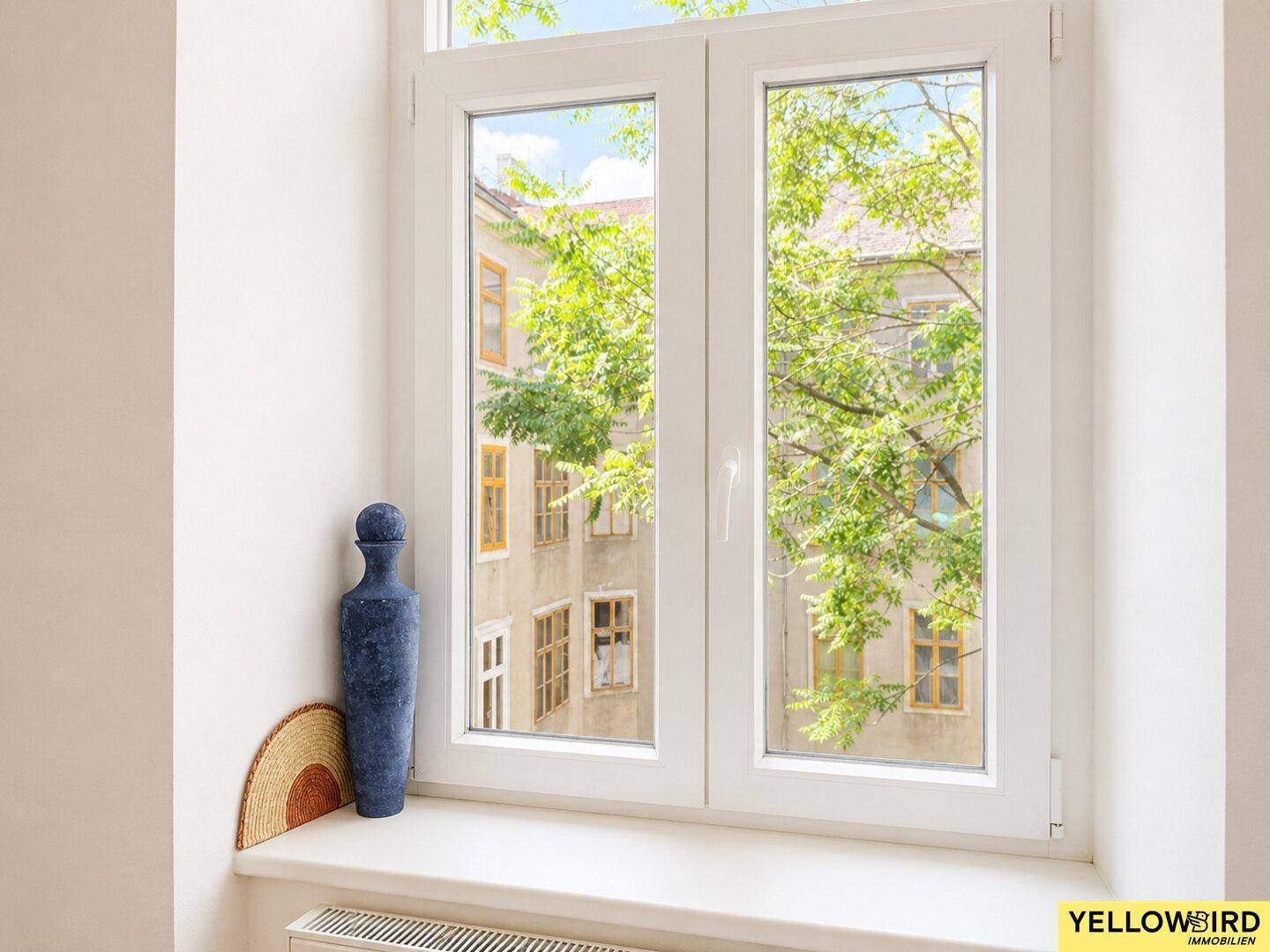 Fenster mit Blick auf einen grünen Innenhof und die umliegenden Gebäude.
