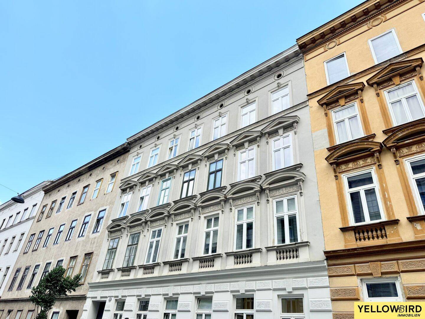 Historische Fassade eines Mehrfamilienhauses mit vielen Fenstern und architektonischen Details.