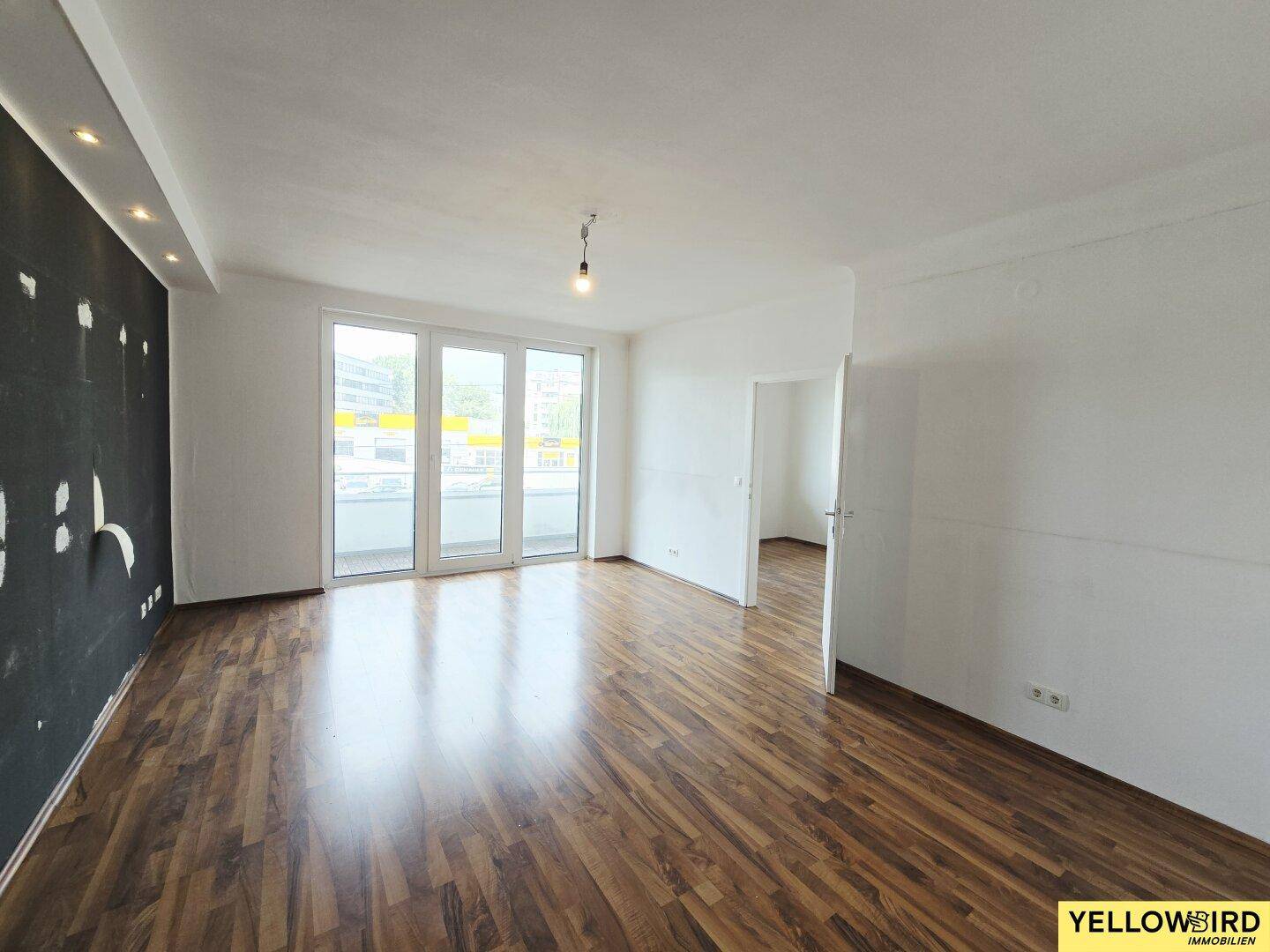 Geräumiges Wohnzimmer mit Laminatboden, weiß gestrichenen Wänden und Zugang zu einem Balkon.