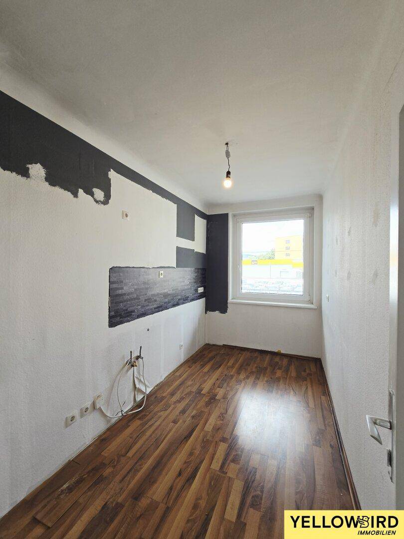 Leere Küche mit Laminatboden und vorbereiteten Anschlüssen, bereit für die Installation einer Einbauküche.