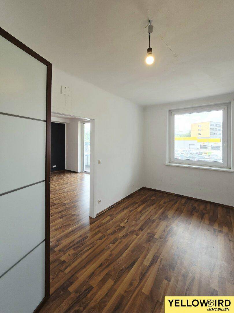 Helles Zimmer mit Laminatboden und einem Fenster, das viel Tageslicht hereinlässt.
