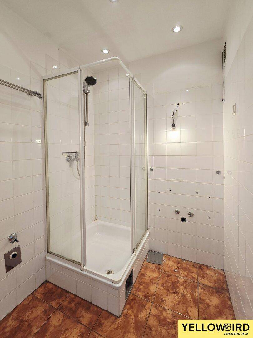 Badezimmer mit Duschkabine, weißen Wandfliesen und braunen Bodenfliesen.