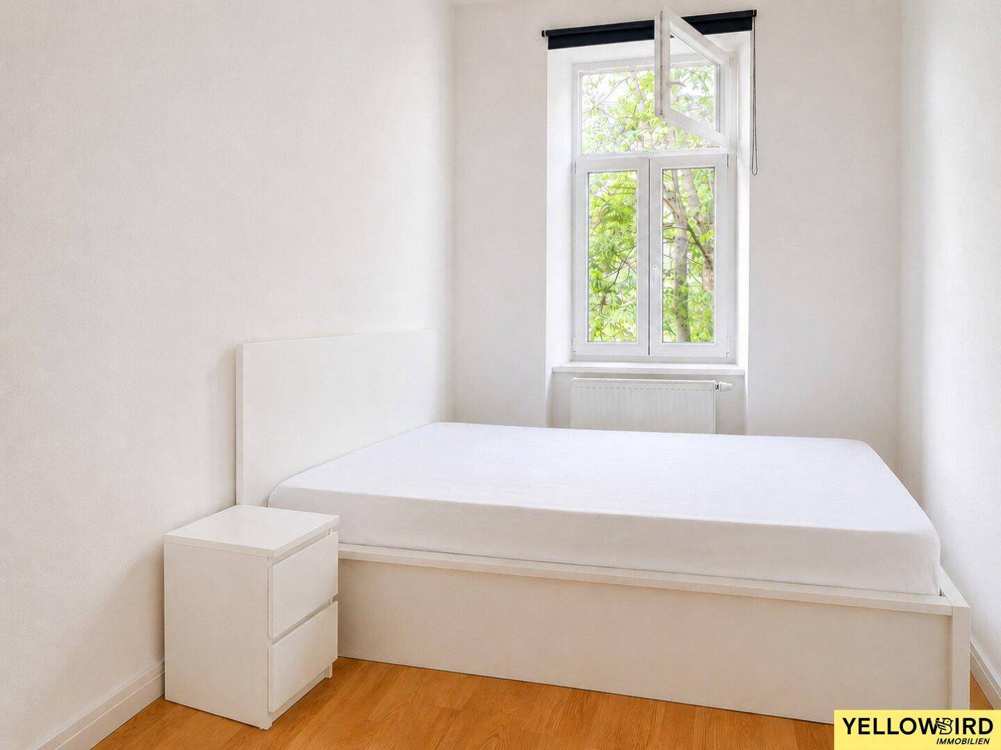 Helles Schlafzimmer mit weißem Bett, Nachttisch und Parkettboden, ideal für erholsame Nächte.