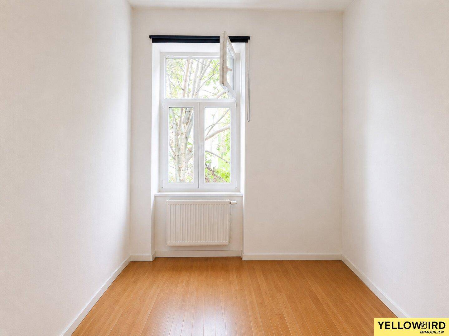 Leeres Zimmer mit Parkettboden und einem Fenster, das den Raum mit Tageslicht erfüllt.