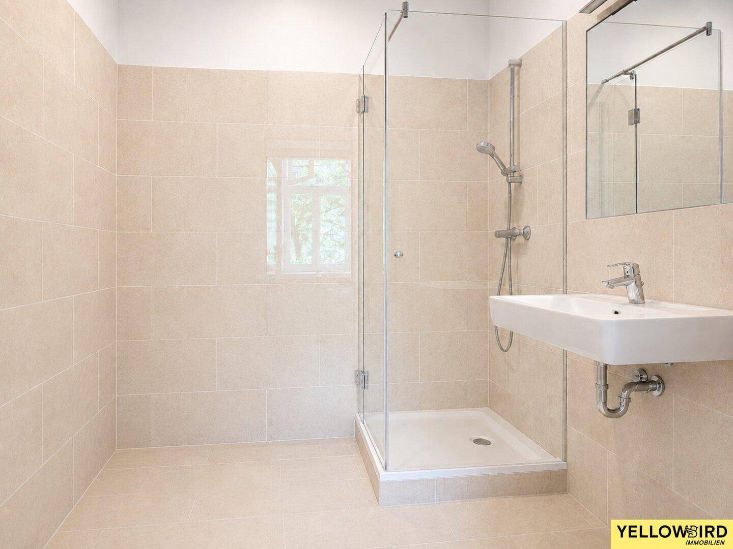 Modernes Badezimmer mit beigefarbenen Fliesen, Duschkabine und Waschbecken, hell und geräumig.